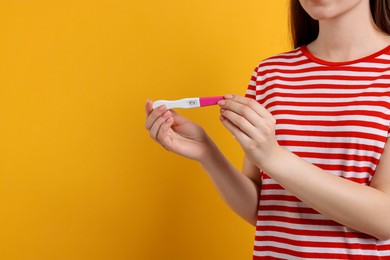 Woman holding pregnancy test on orange background, closeup. Space for text