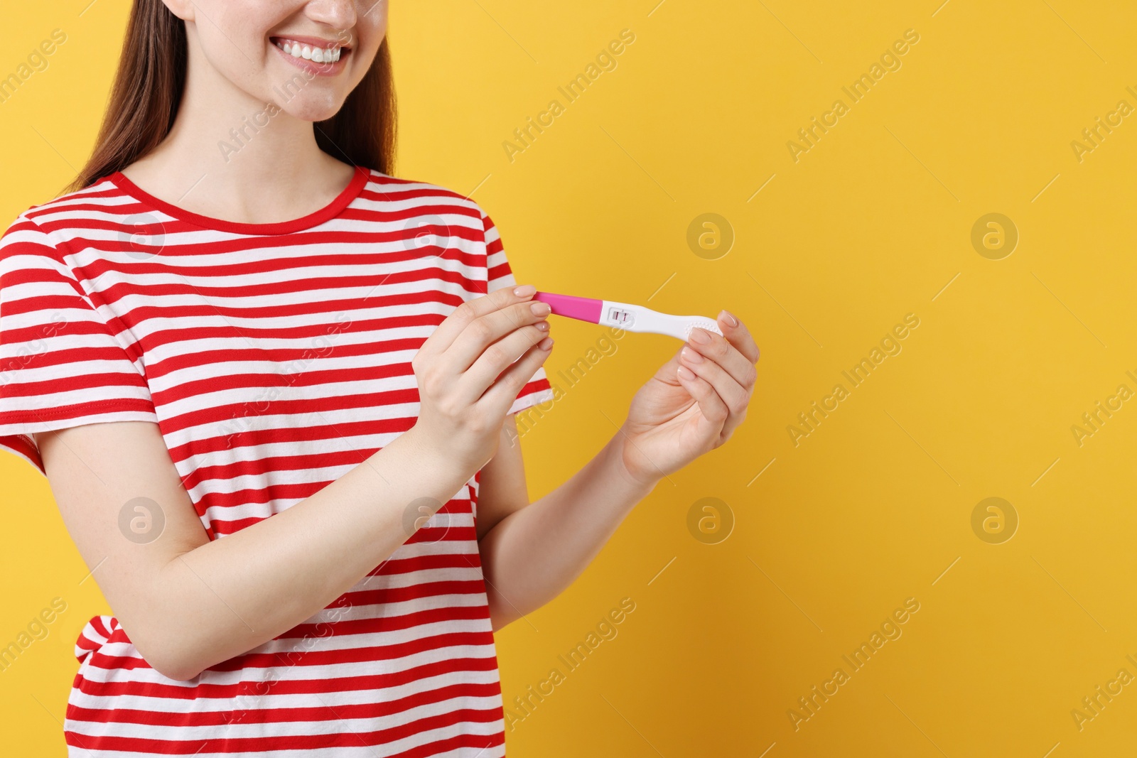 Photo of Woman holding pregnancy test on orange background, closeup. Space for text