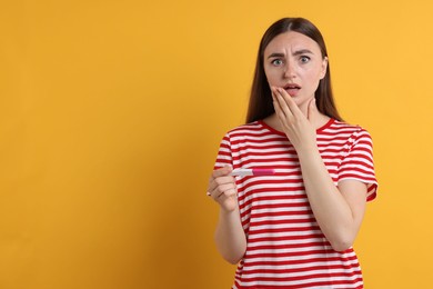 Shocked woman holding pregnancy test on orange background, space for text