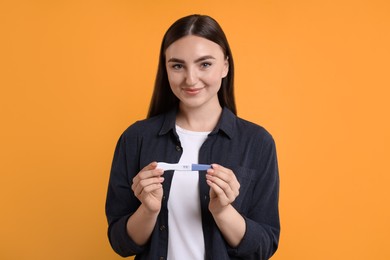 Photo of Happy woman holding pregnancy test on orange background