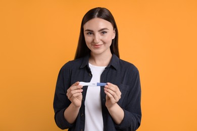 Happy woman holding pregnancy test on orange background