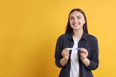 Happy woman holding pregnancy test on orange background, space for text