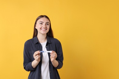 Happy woman holding pregnancy test on orange background, space for text