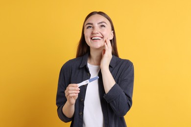 Photo of Happy woman holding pregnancy test on orange background