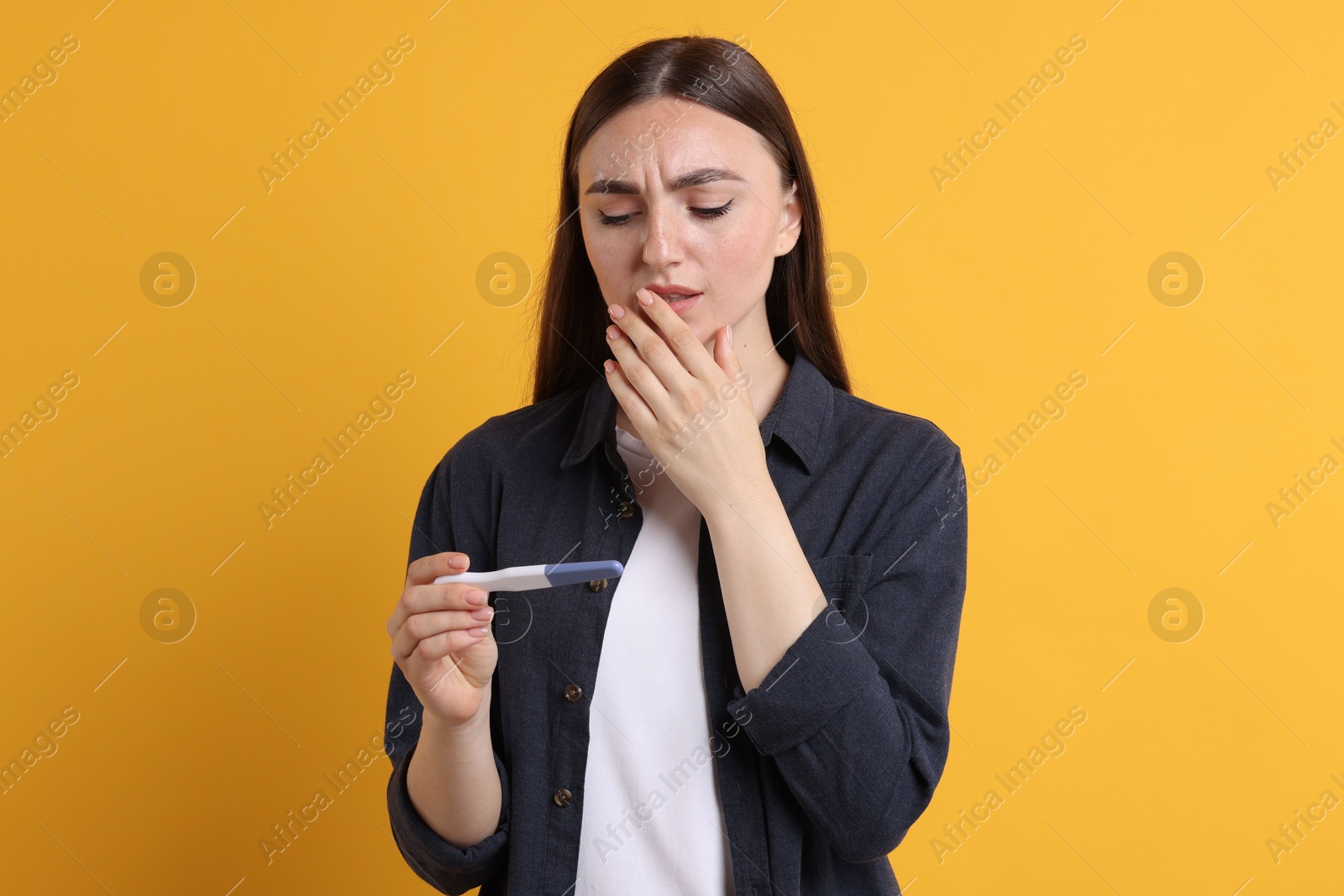 Photo of Sad woman holding pregnancy test on orange background