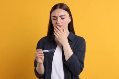 Sad woman holding pregnancy test on orange background