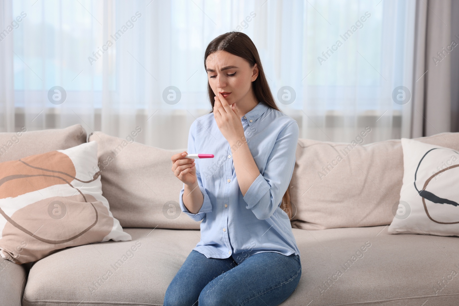 Photo of Sad woman holding pregnancy test on sofa indoors