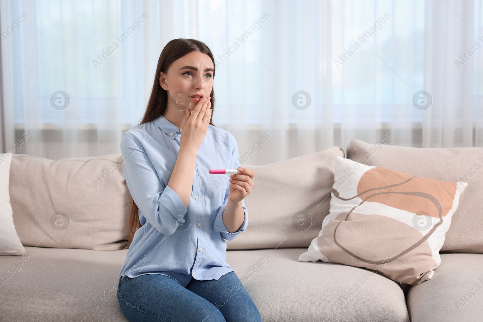 Photo of Sad woman holding pregnancy test on sofa indoors