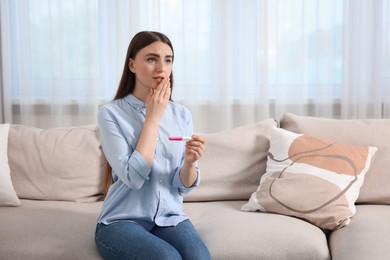 Sad woman holding pregnancy test on sofa indoors