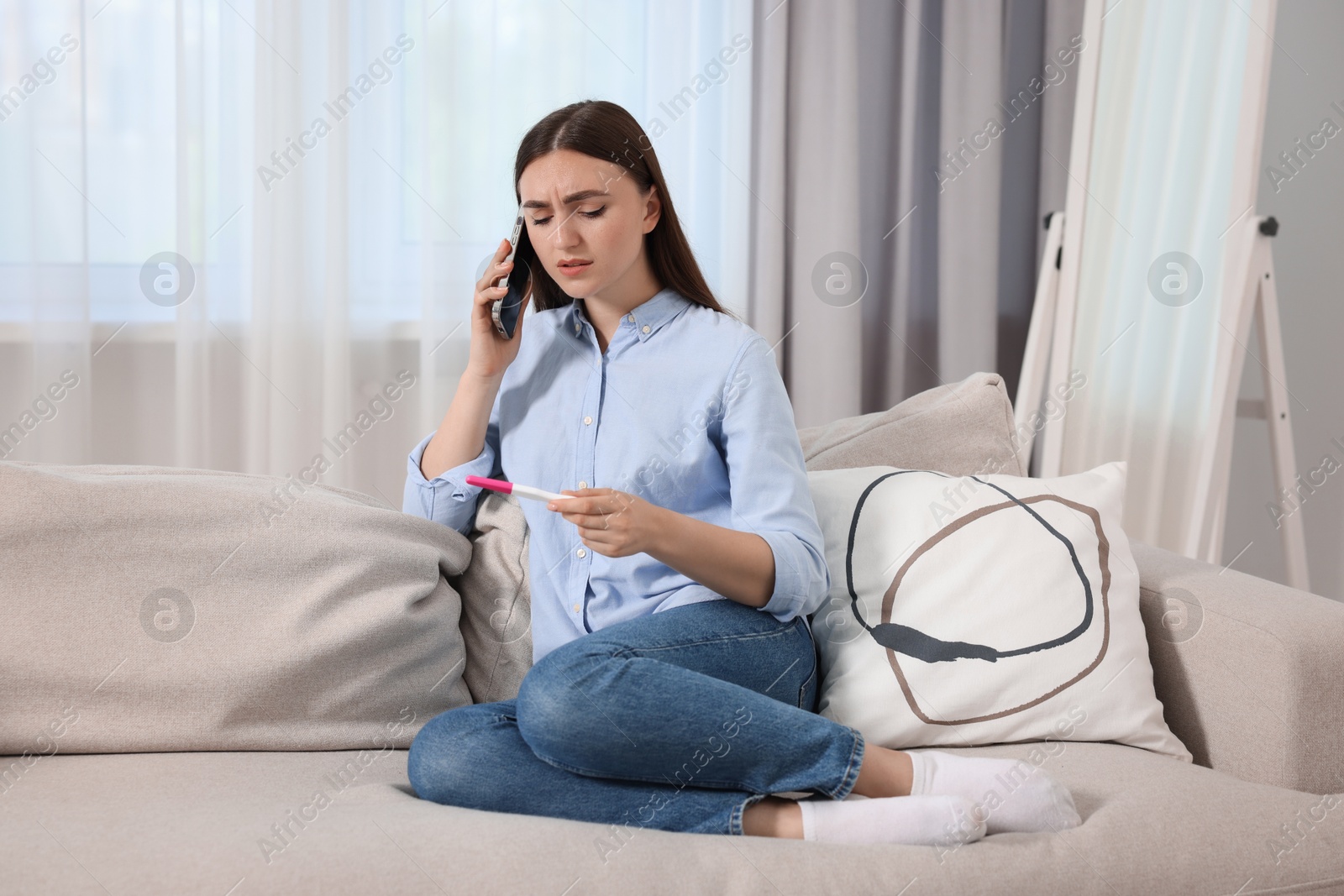 Photo of Sad woman with pregnancy test talking on smartphone indoors