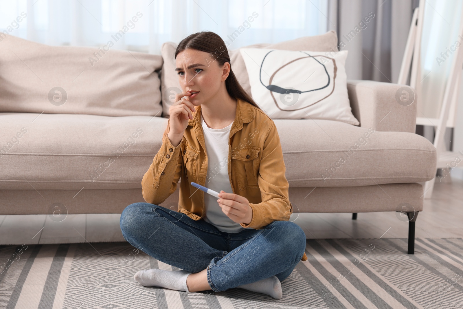 Photo of Sad woman holding pregnancy test on floor indoors