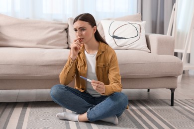 Sad woman holding pregnancy test on floor indoors