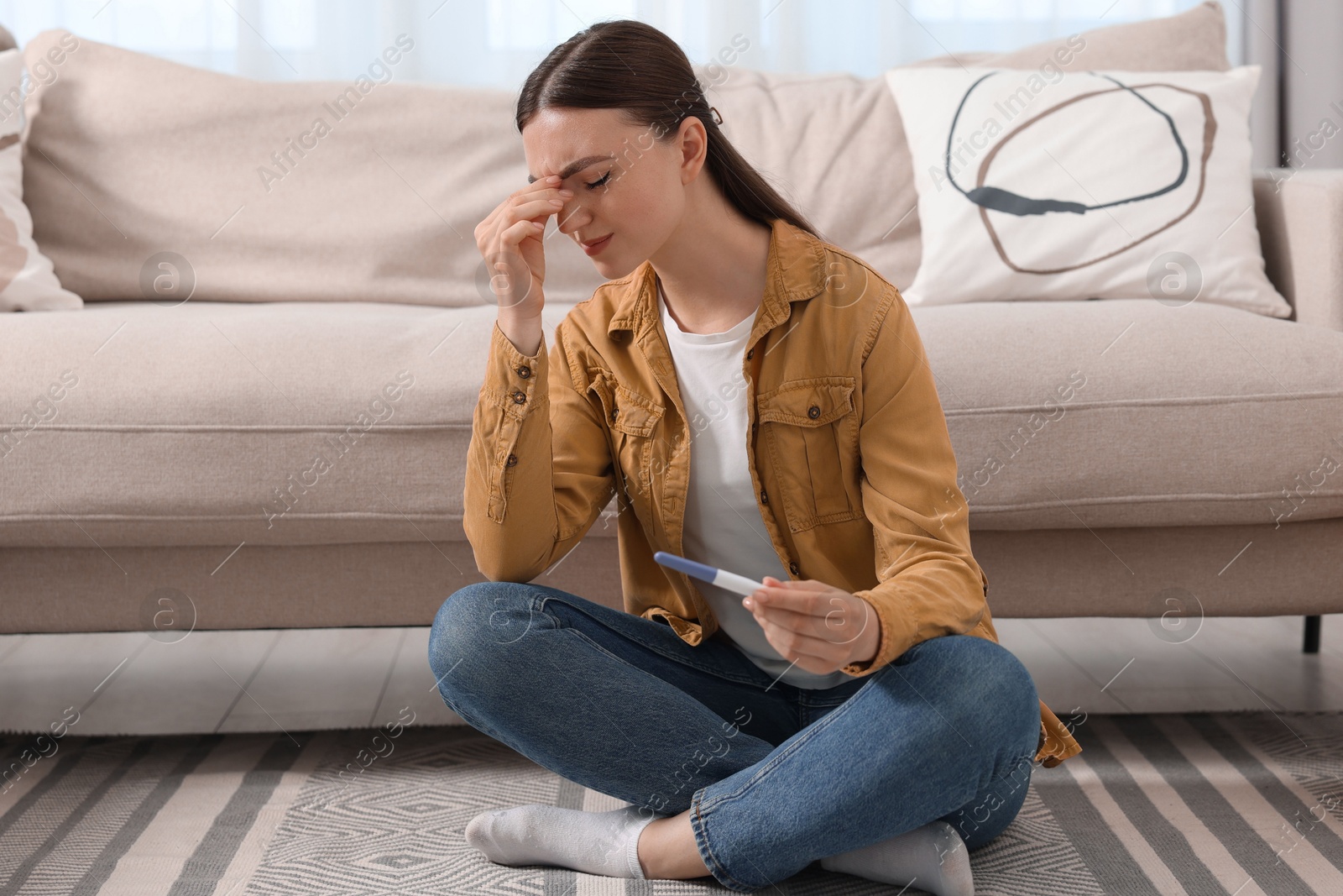 Photo of Sad woman holding pregnancy test on floor indoors