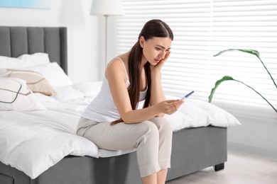 Photo of Sad woman holding pregnancy test on bed in room