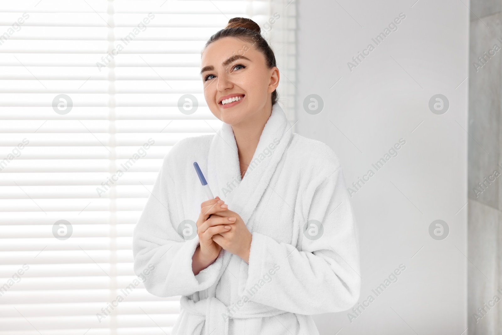 Photo of Happy woman holding pregnancy test in bathroom