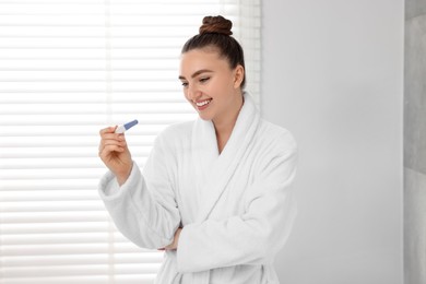 Photo of Happy woman holding pregnancy test in bathroom