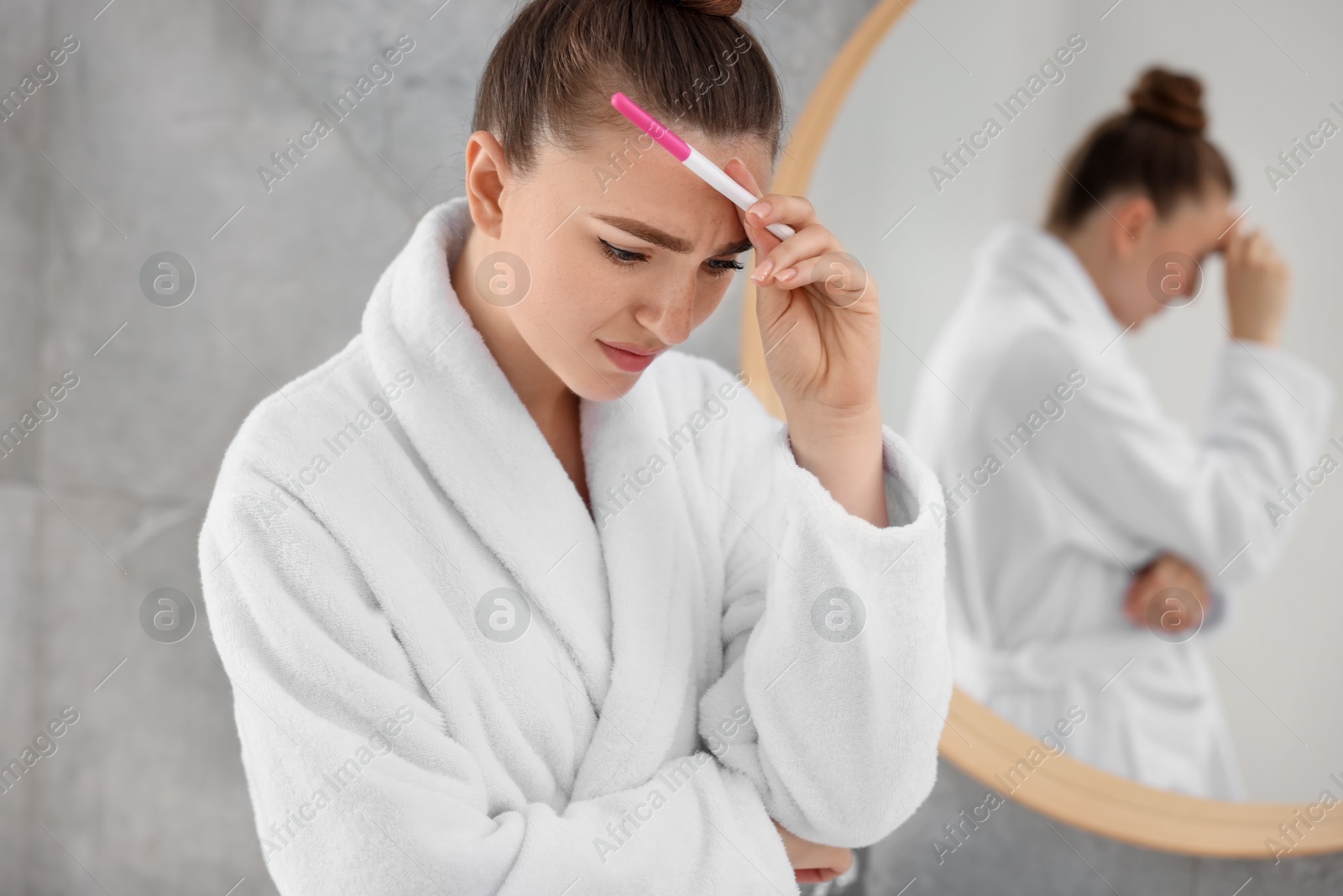 Photo of Sad woman holding pregnancy test in bathroom