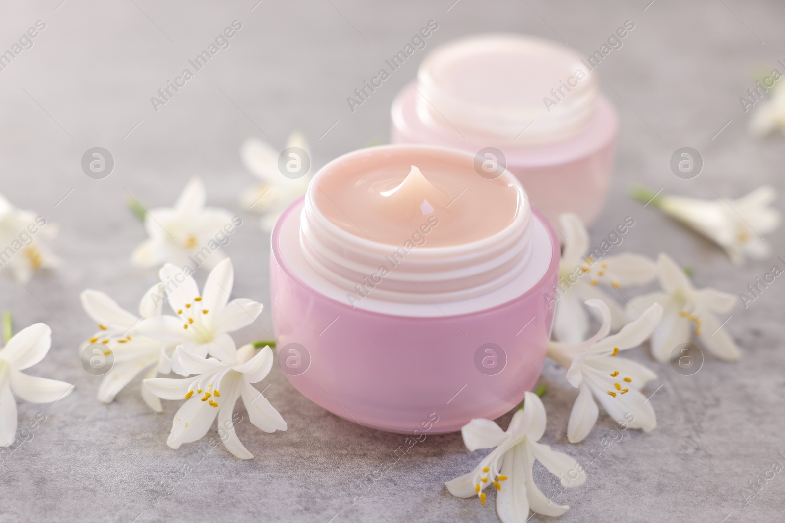 Photo of Cream in jars and beautiful jasmine flowers on grey table, closeup