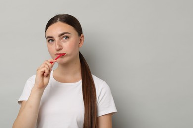 Beautiful woman brushing her teeth on gray background, space for text