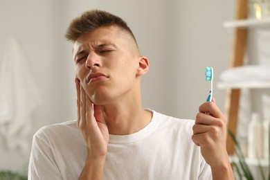 Young man with toothbrush suffering from toothache in bathroom