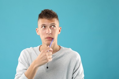 Young man brushing his teeth on light blue background