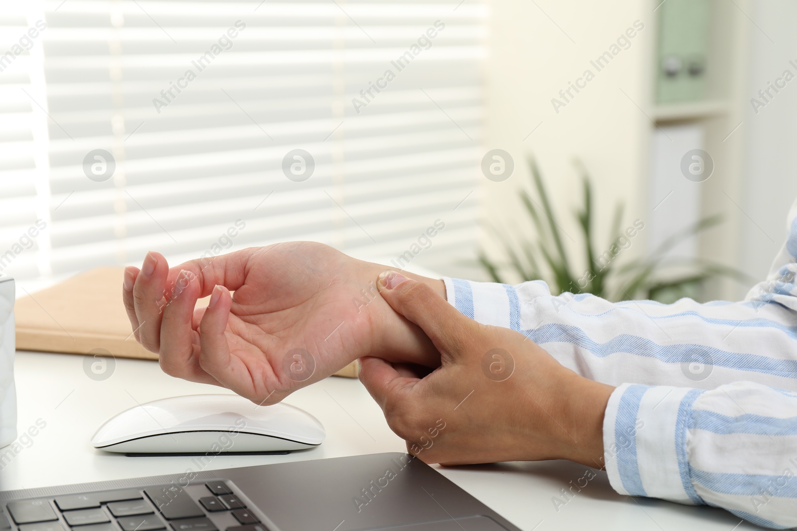 Photo of Carpal tunnel syndrome. Woman suffering from pain in wrist at desk indoors, closeup