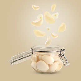 Image of Jar with pickled garlic and cloves falling into it on dark beige background