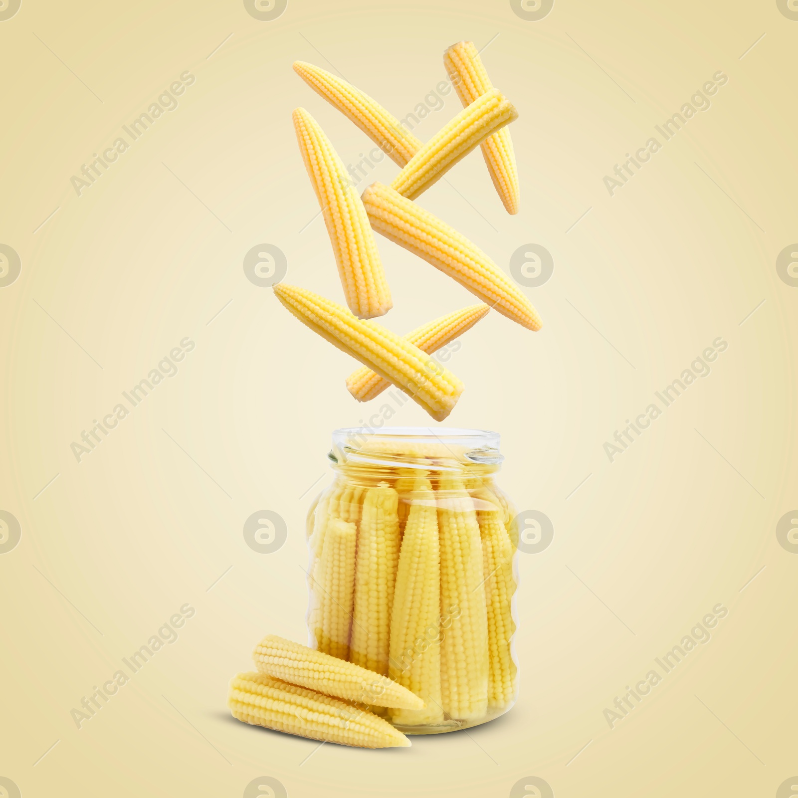 Image of Baby corn cobs falling into jar on light yellow background