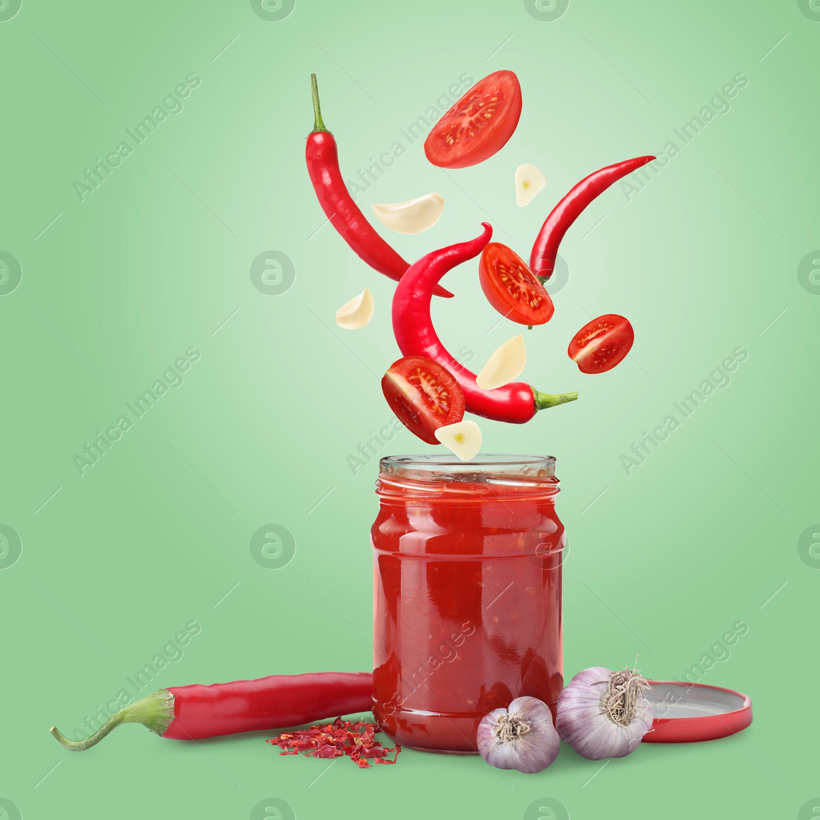 Image of Jar with spicy chili sauce and ingredients falling into it on light green background