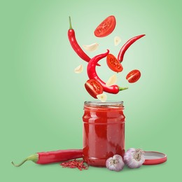 Image of Jar with spicy chili sauce and ingredients falling into it on light green background