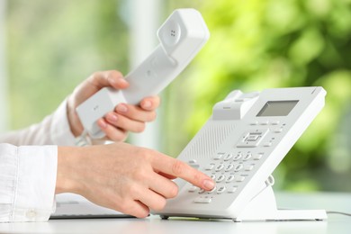 Photo of Assistant dialing number on telephone against blurred green background, closeup