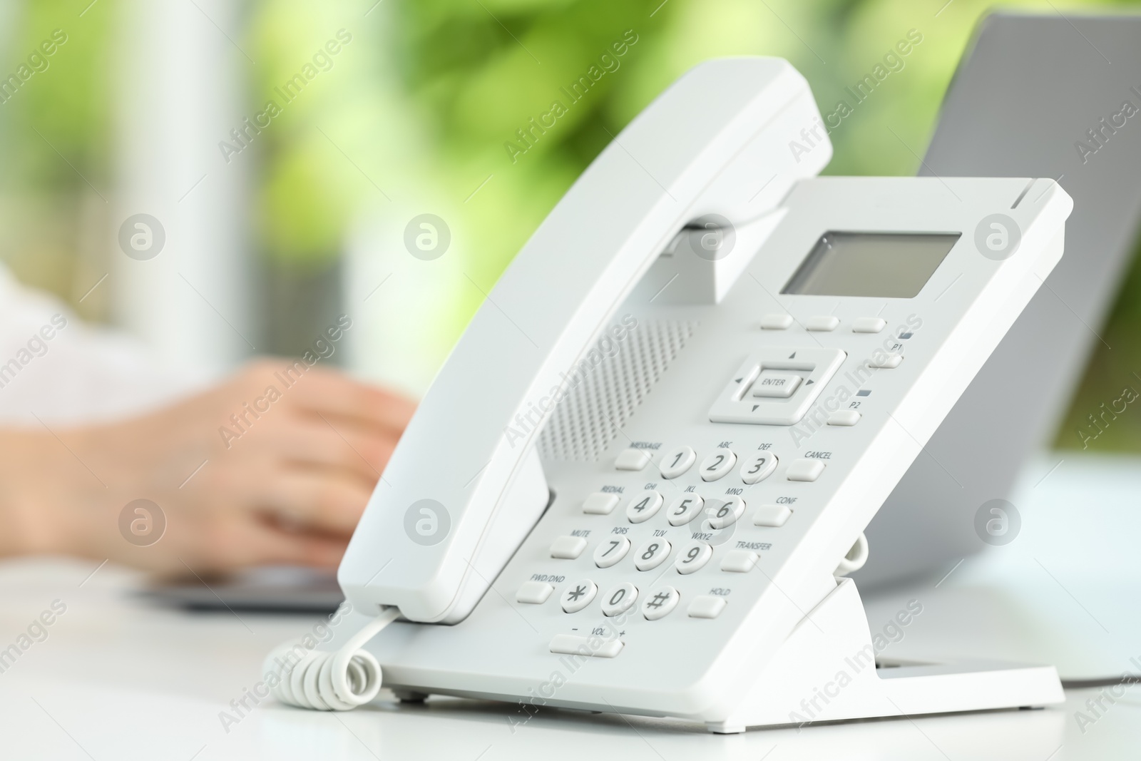 Photo of White telephone on table against blurred background, selective focus