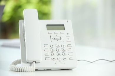 Photo of White telephone on table against blurred background, closeup