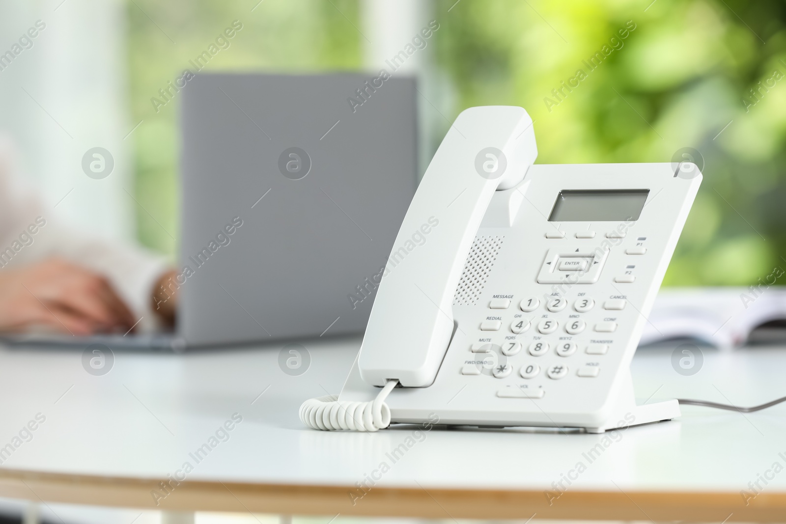 Photo of White telephone on table against blurred background, selective focus