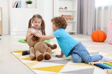 Photo of Cute little children playing with teddy bear on floor in kindergarten