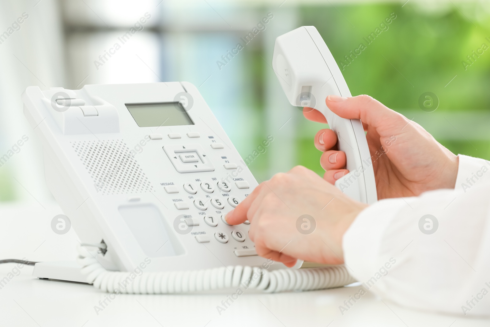 Photo of Assistant dialing number on telephone at white table, closeup