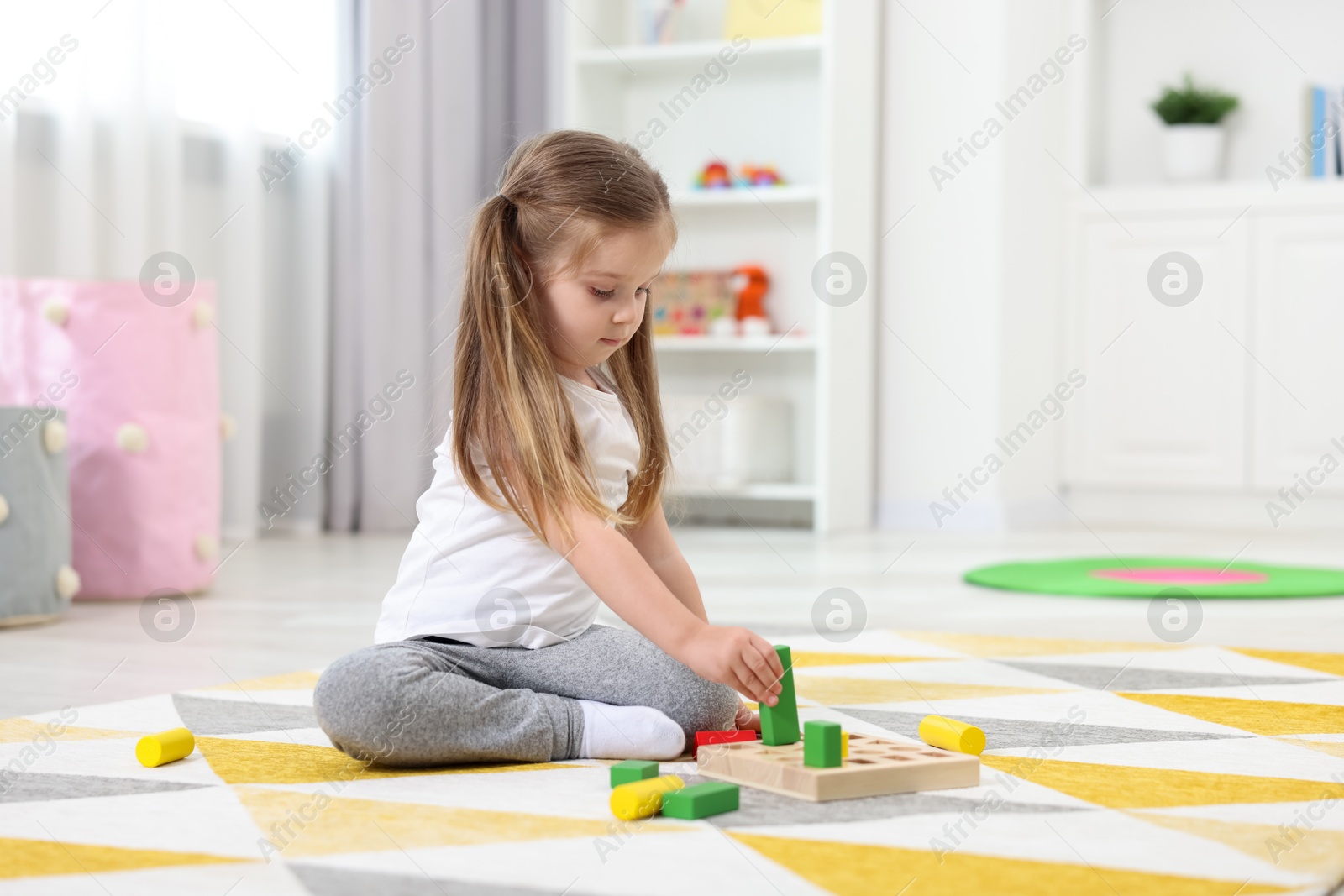 Photo of Cute little girl playing with set of wooden geometric figures on floor in kindergarten. Space for text