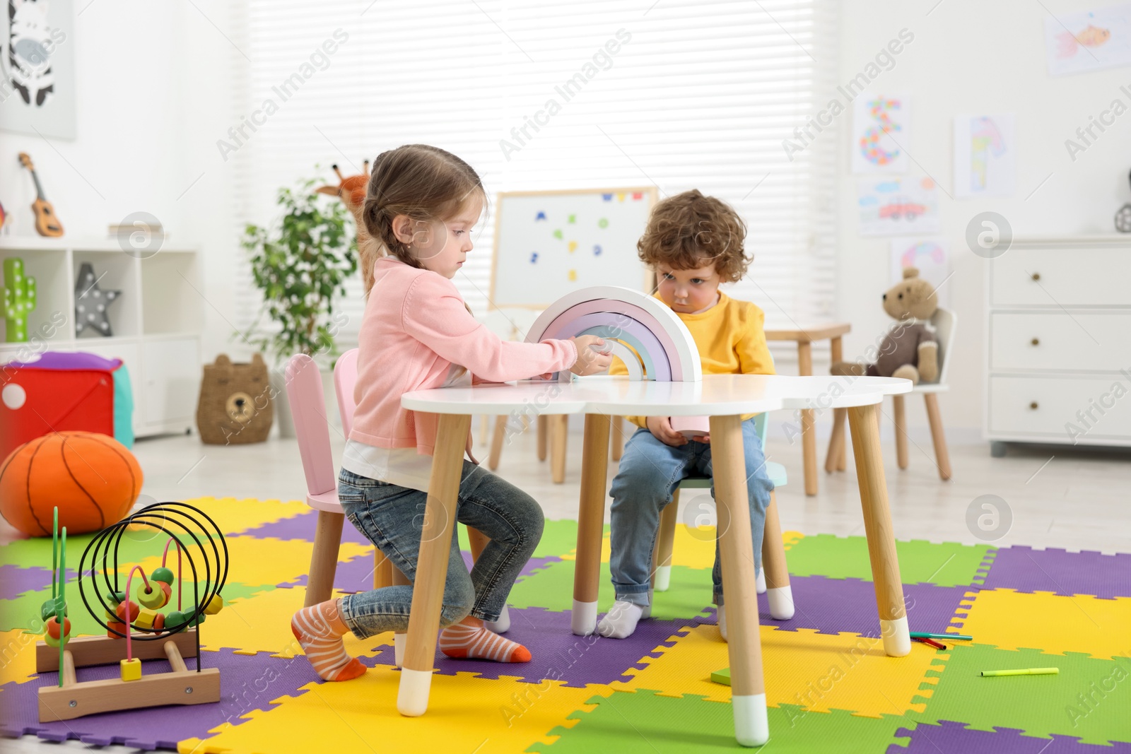 Photo of Cute little children playing with colorful toy rainbow at white table in kindergarten