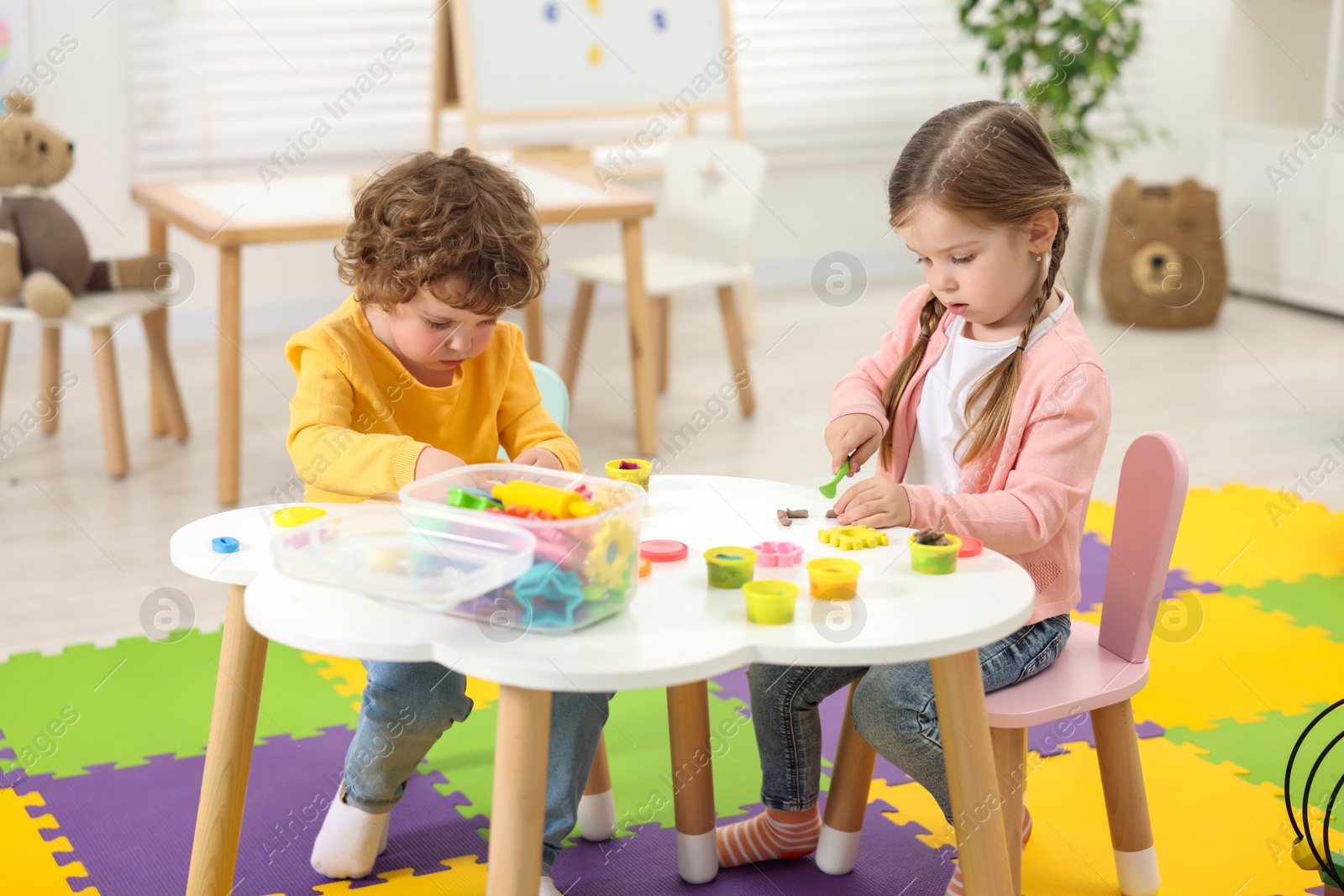 Photo of Cute little children modeling from plasticine at white table in kindergarten