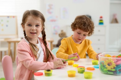 Photo of Cute little children modeling from plasticine at white table in kindergarten