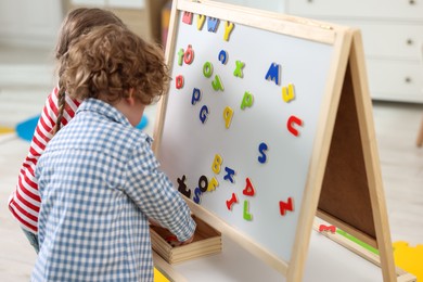 Cute little children learning alphabet with magnetic letters on board in kindergarten