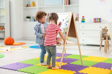 Little children learning alphabet with magnetic letters on board in kindergarten