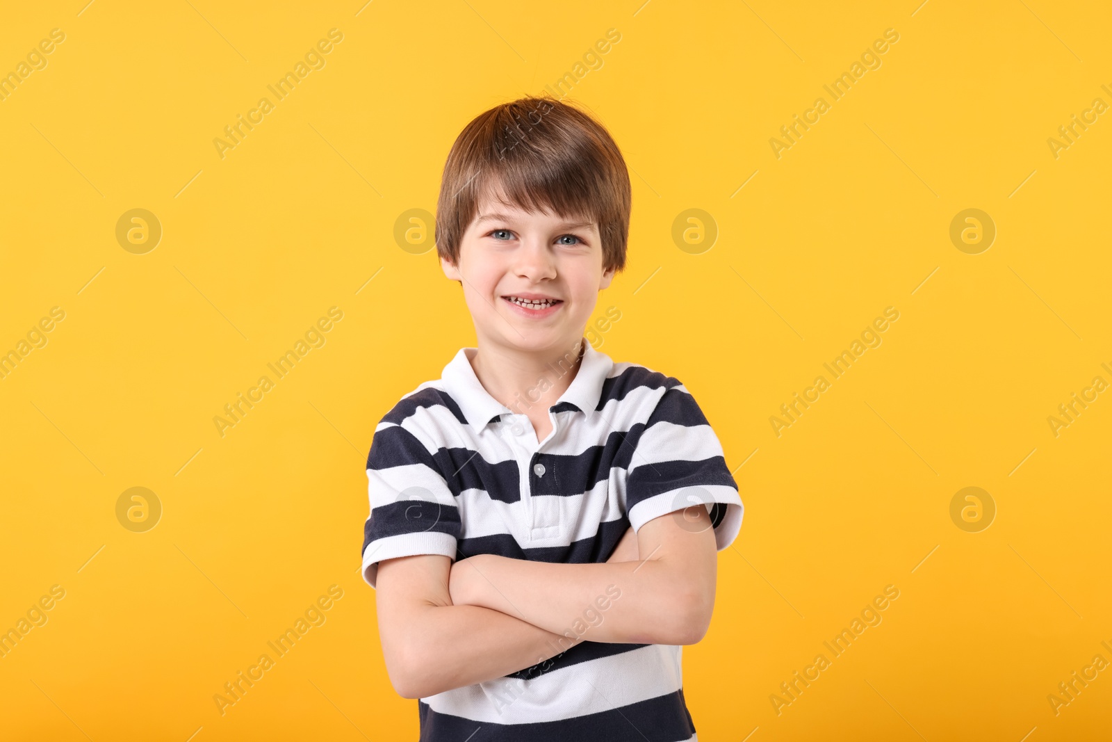 Photo of Portrait of cute little boy with crossed arms on orange background