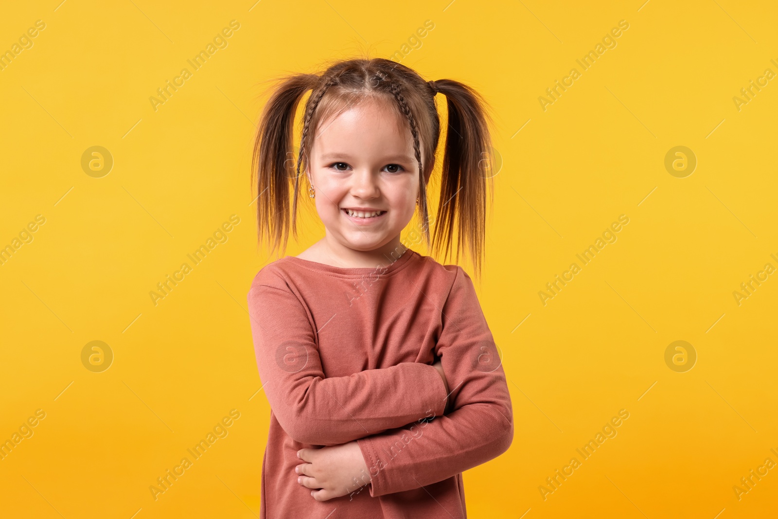 Photo of Portrait of cute little girl with crossed arms on orange background