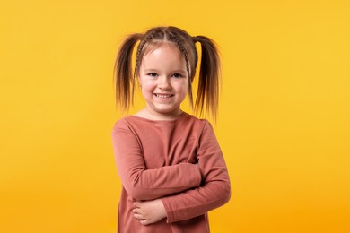 Photo of Portrait of cute little girl with crossed arms on orange background