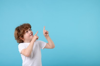 Photo of Cute little boy pointing at something on light blue background, space for text