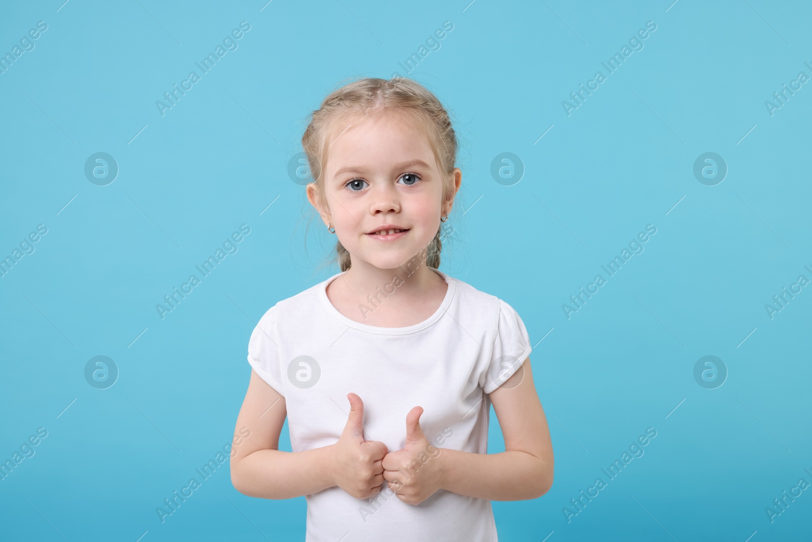 Photo of Cute little girl showing thumbs up on light blue background