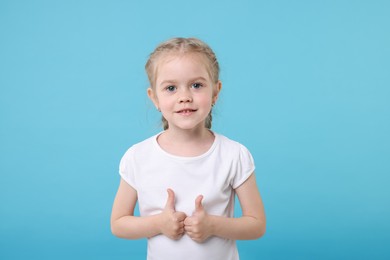 Cute little girl showing thumbs up on light blue background