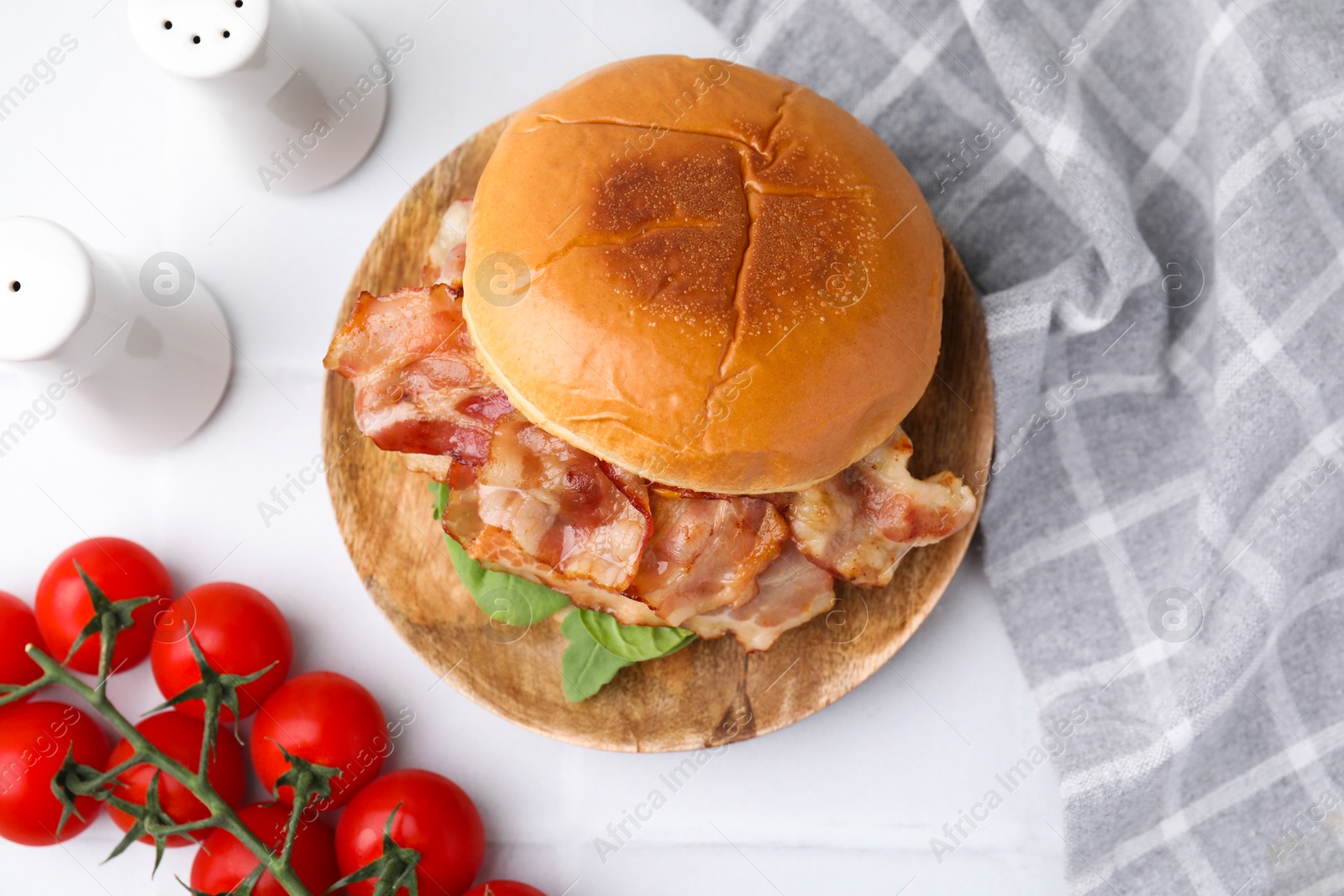 Photo of Delicious burger with bacon, greens and tomatoes on white table, flat lay