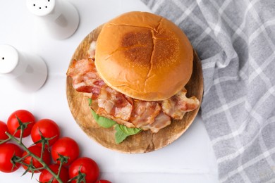 Photo of Delicious burger with bacon, greens and tomatoes on white table, flat lay